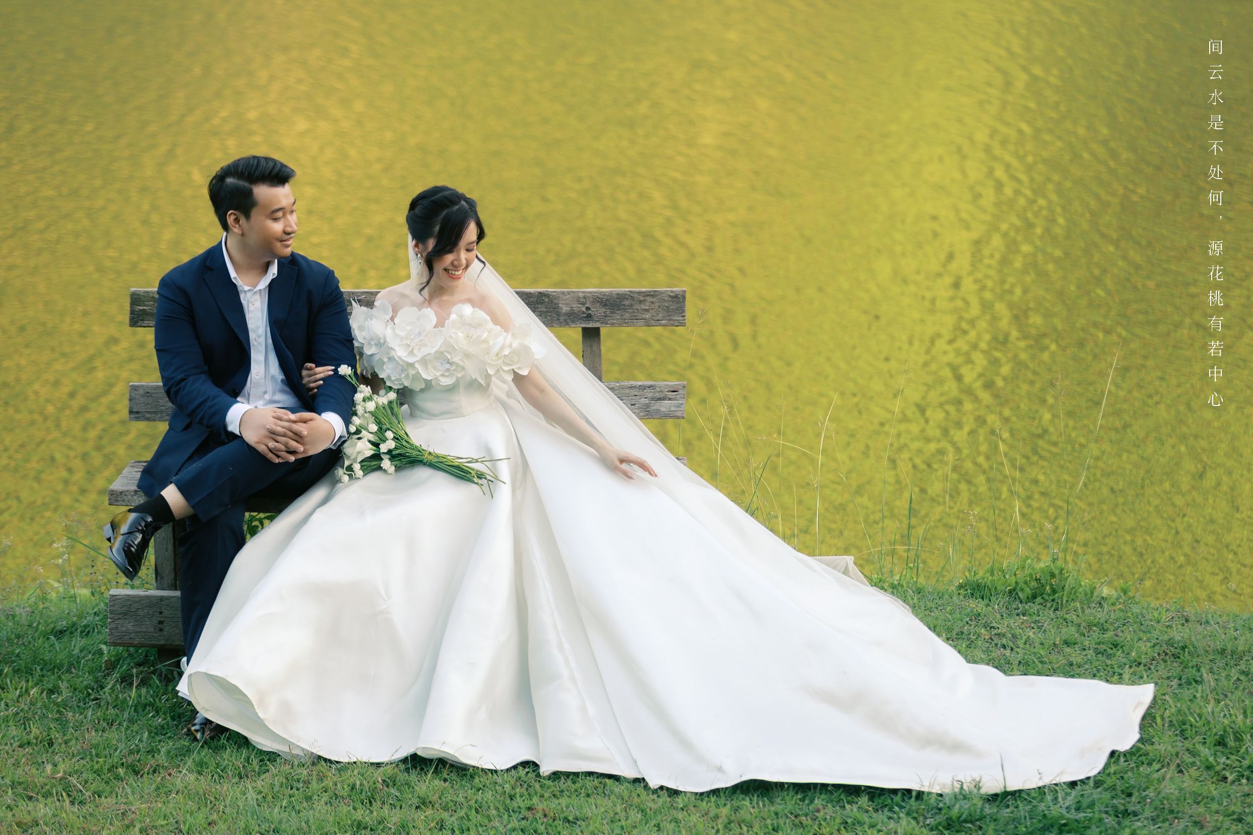 A bride in ivory gown satin flowers with a long train and a groom wearing navy blue suit